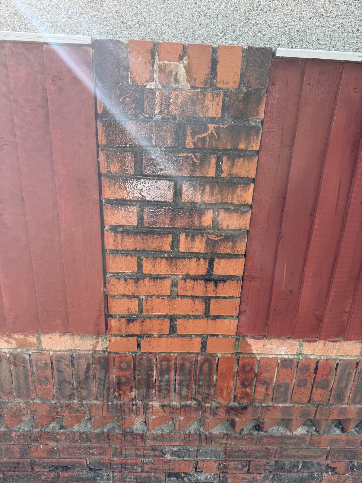 Brick pillar being pressure washed beside a red timber fence